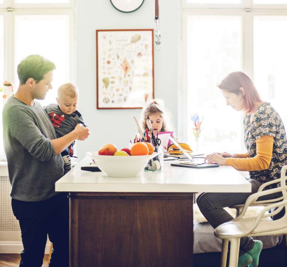A white man and woman gather around their kitchen island with their two children.
