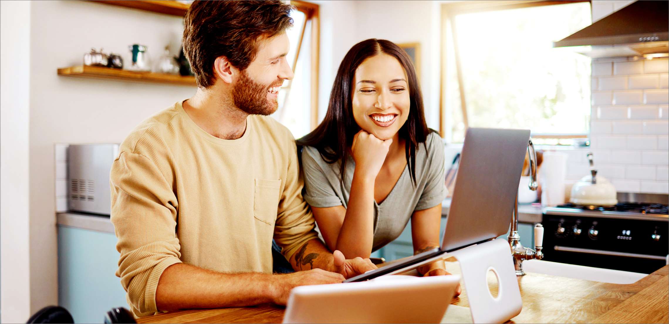 Happy young man working on laptop while his wife stands next to him looking at the screen.