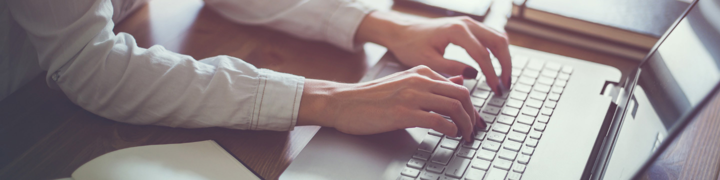 Close up of a woman's hands with red painted nails typing on a computer laptop keyboard