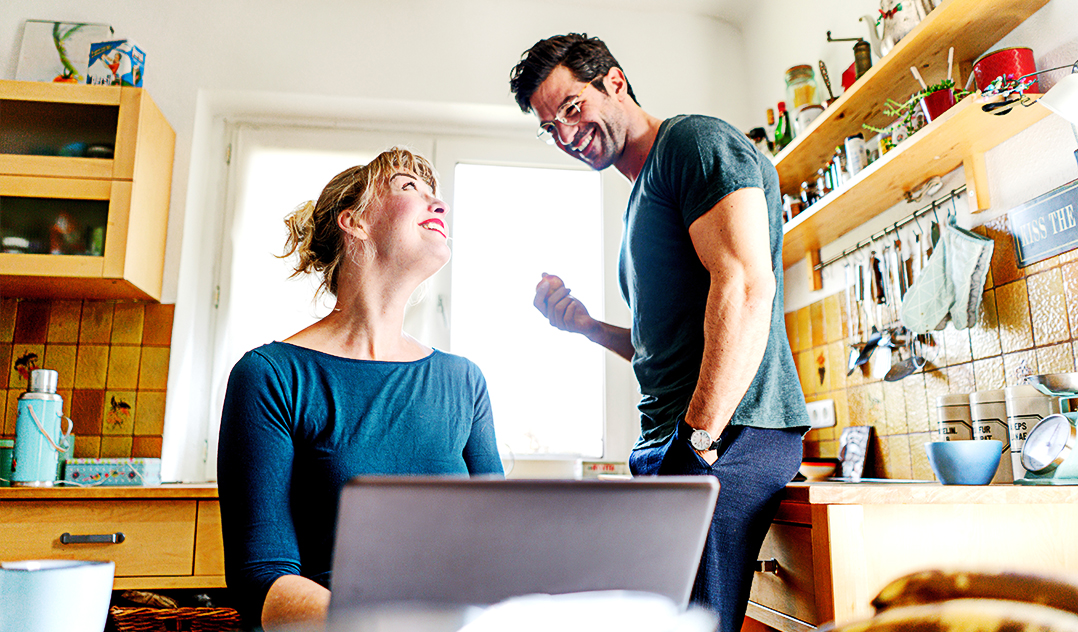 A couple in their kitchen smile at one another