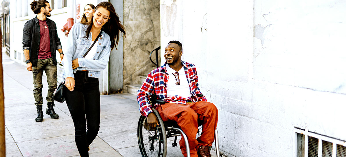 man in wheelchair smiling looking at his friend walking beside him