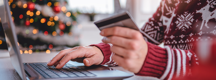 Woman in Christmas sweater sitting at a laptop with credit card in hand