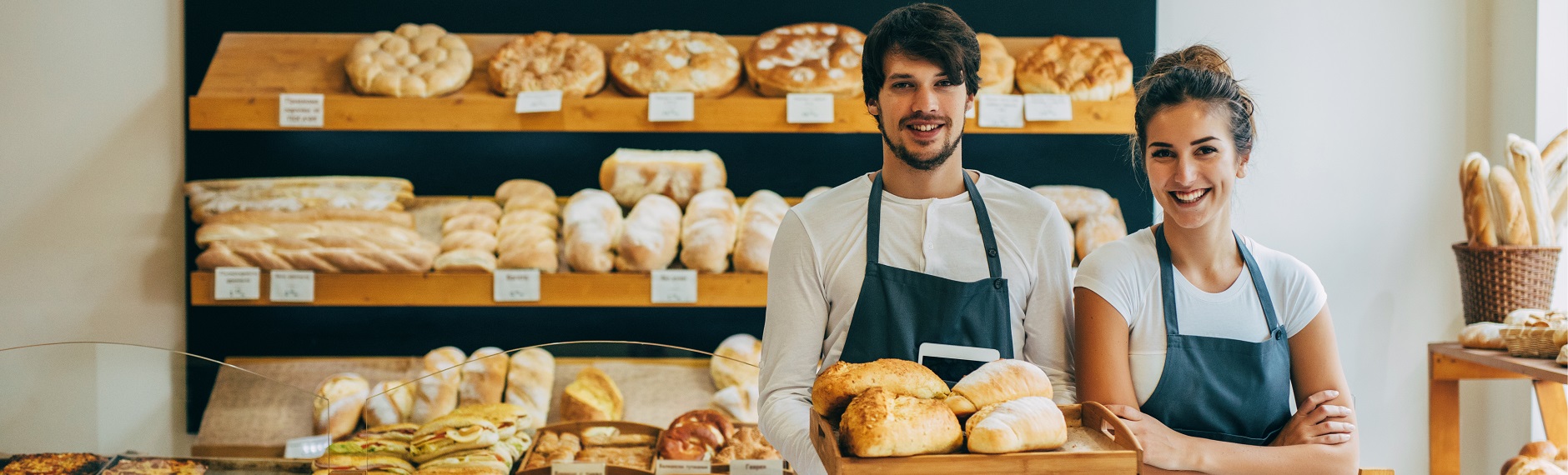 Two smiling bakery owners in front of a wall of bread