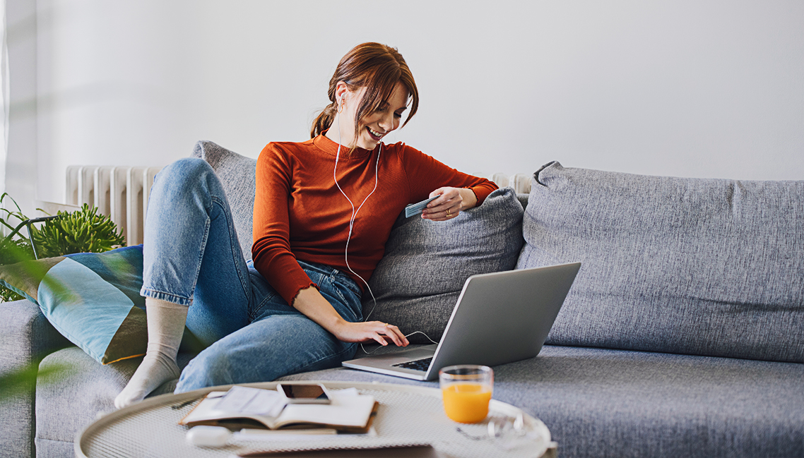 Young woman on a sofa at home, using her laptop with headphones on