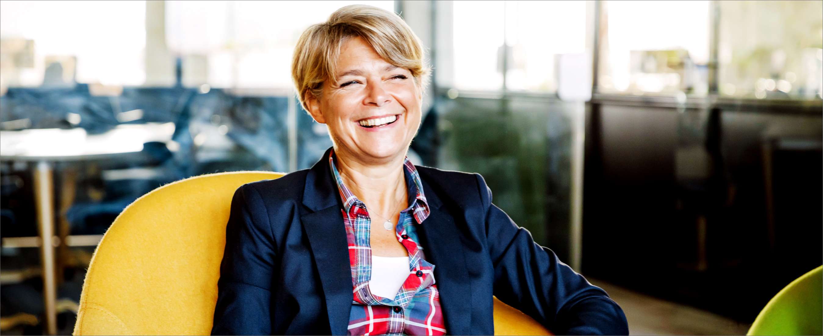 A woman sitting in a yellow chair in a modern office environment smiling.