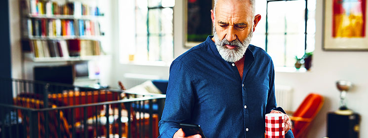 Older man at home looking at his cellphone with a concerned look on his face