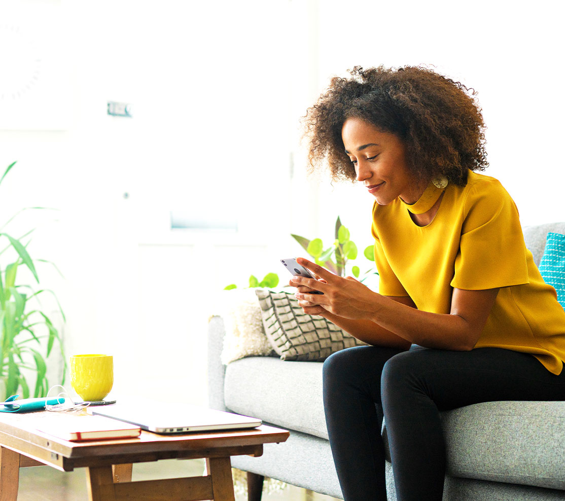 A young woman sits on her sofa, working on her phone 