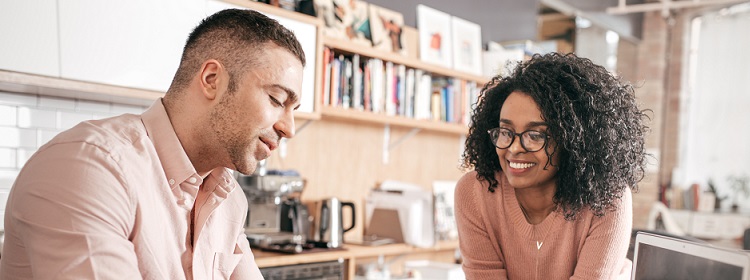 A smiling man and woman sitting in their kitchen with a laptop