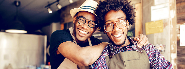 Two young business owners smiling; one puts an arm around his business partners' shoulder.