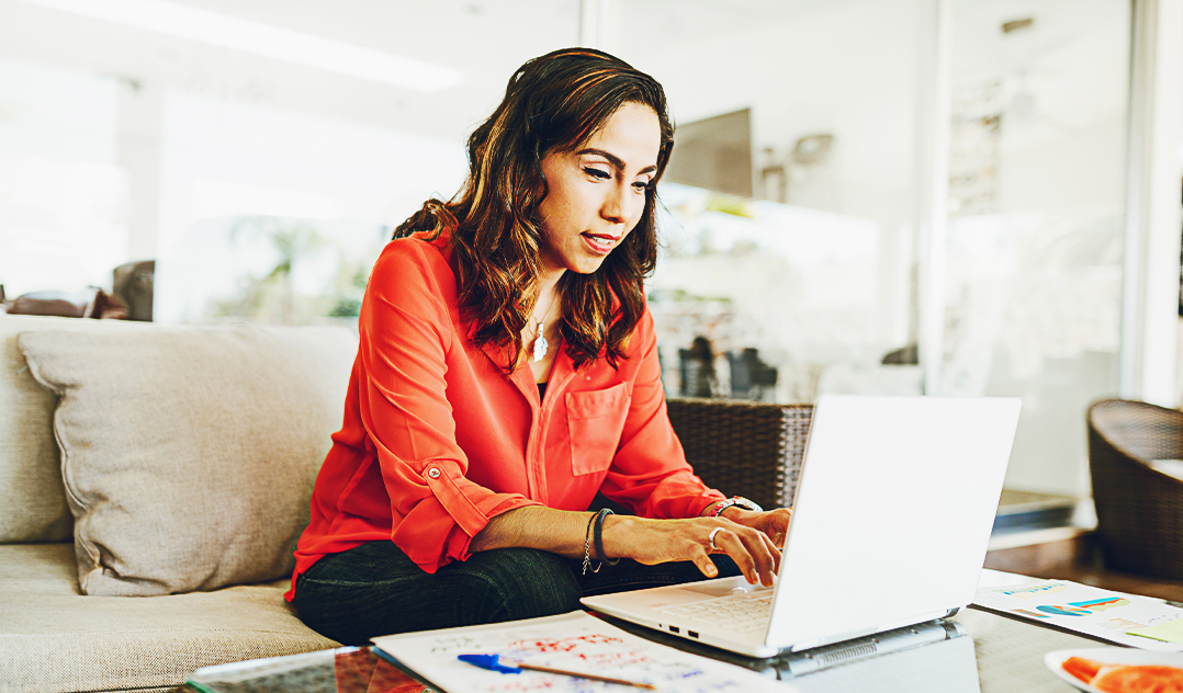 A young woman site on a sofa at home, working at her laptop