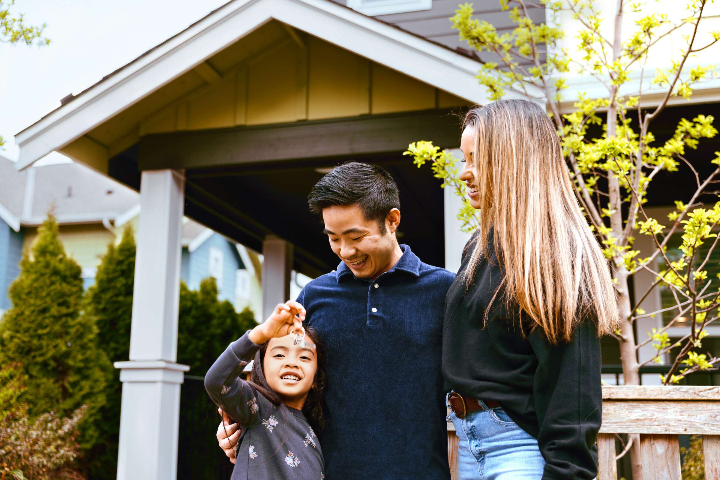 A mixed race husband, wife, and their daughter hold up the keys to their new house, smiling with joy and excitement at their investment