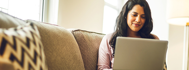 Young woman on a sofa, smiling, working at laptop