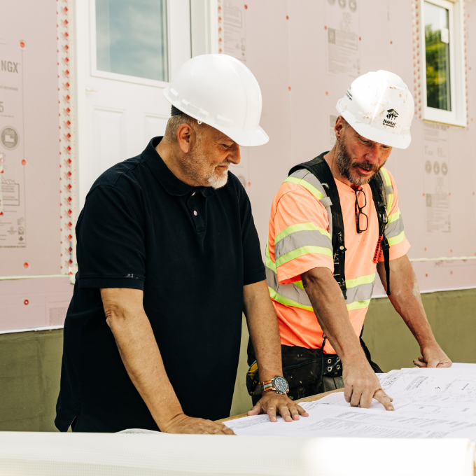 Two men wearing safety gear look over plans at a construction site. Rob C. Meridian Member.