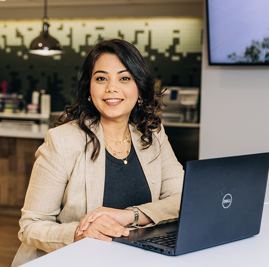 A young female advisor with mid-to-dark skin tone sits at a desk with a laptop. 