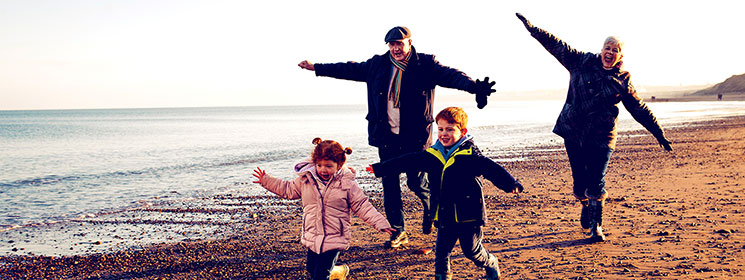 Two grandparents run on the beach with their grandchildren.