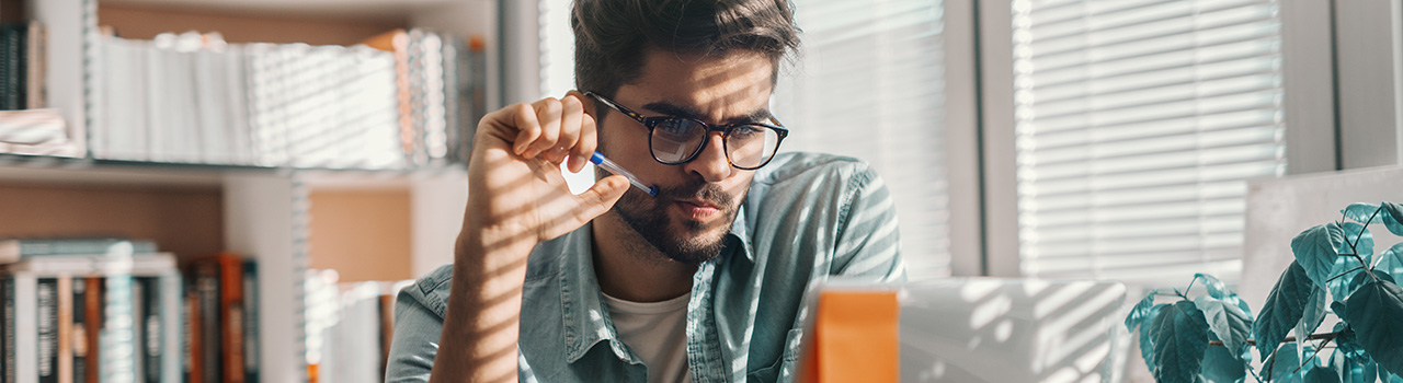Young man with a pen looking at a laptop