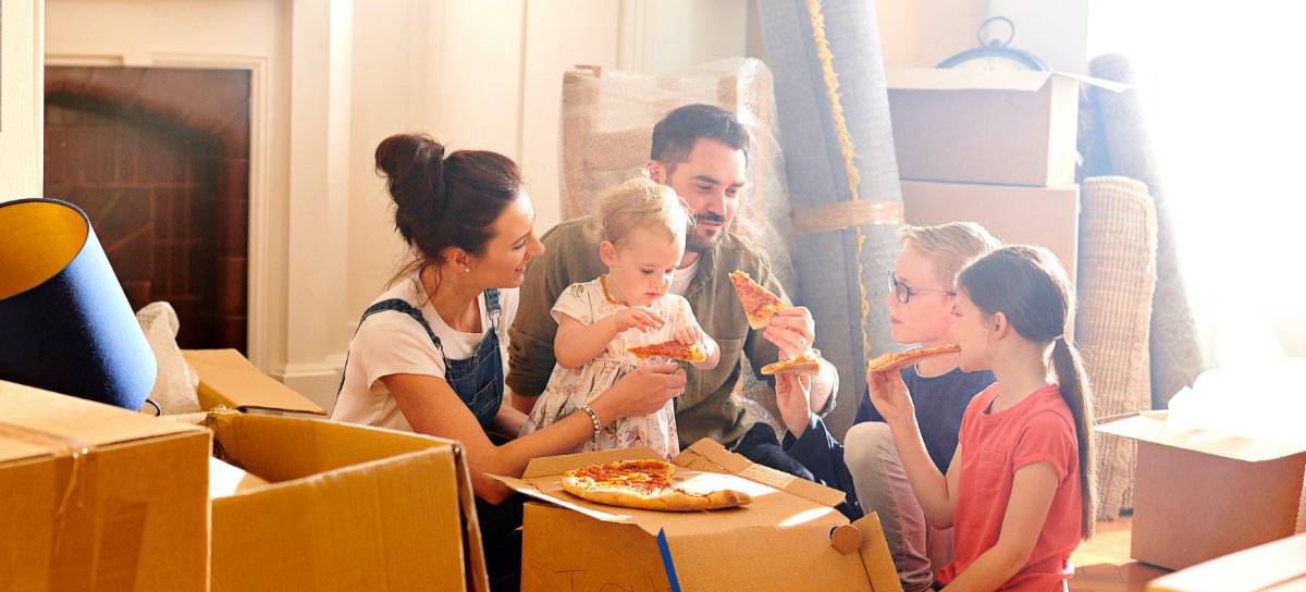 family eating pizza off of a cardboard box in the house they just moved into