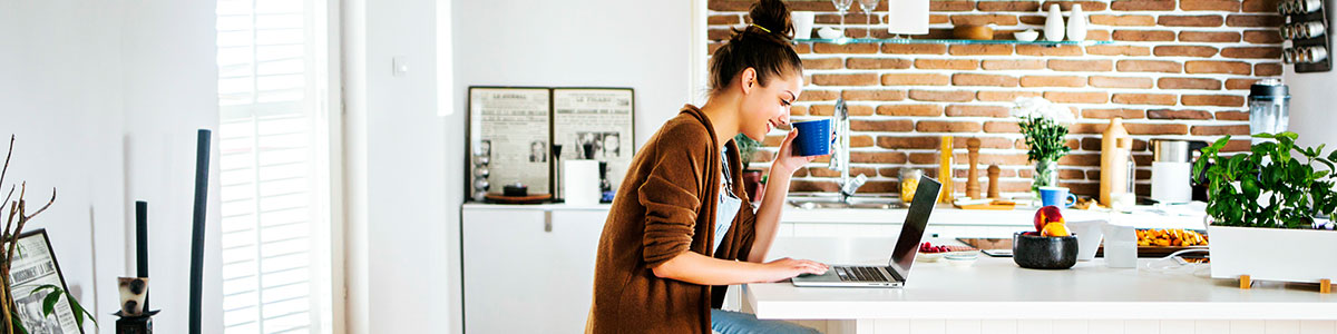 Smiling young woman working on her laptop in a kitchen