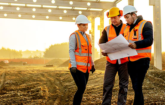 Three coworkers wearing safety gear at a construction site looking at a blueprint plan
