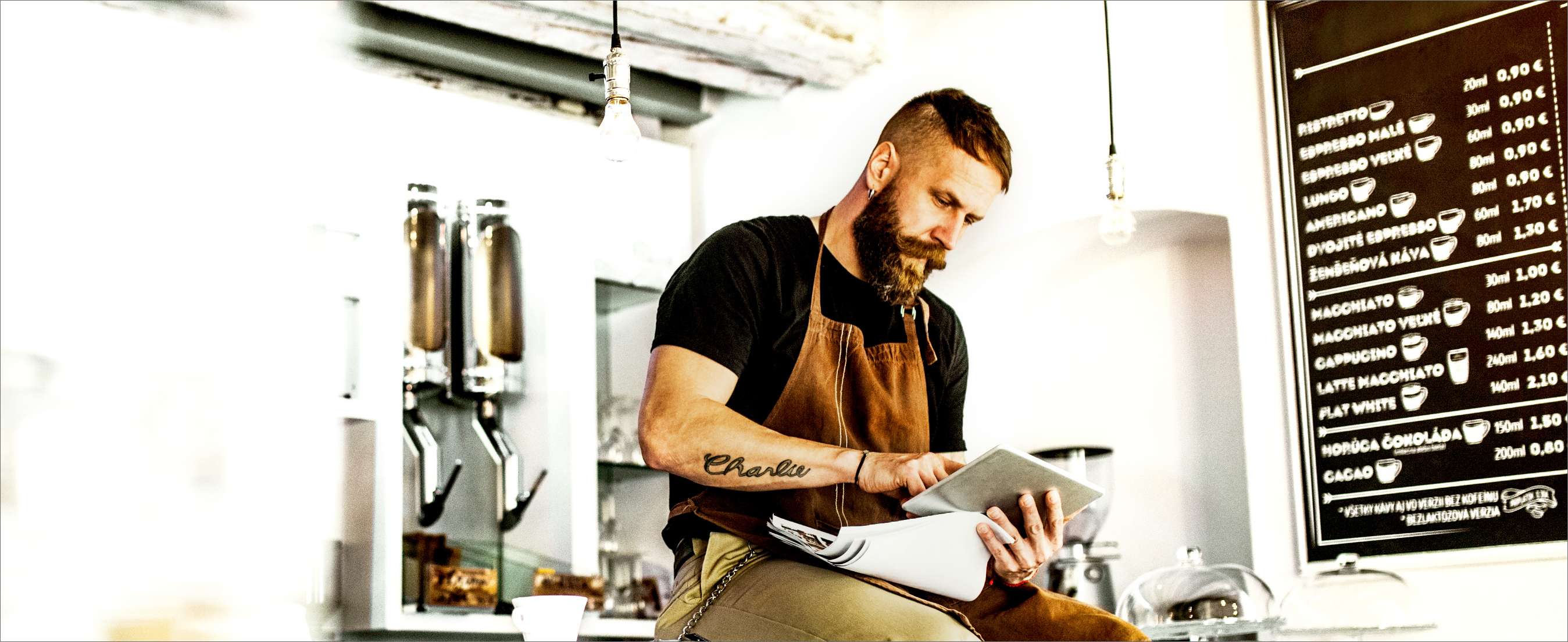 Portrait of a business owner sitting on a counter in a cafe, using tablet.