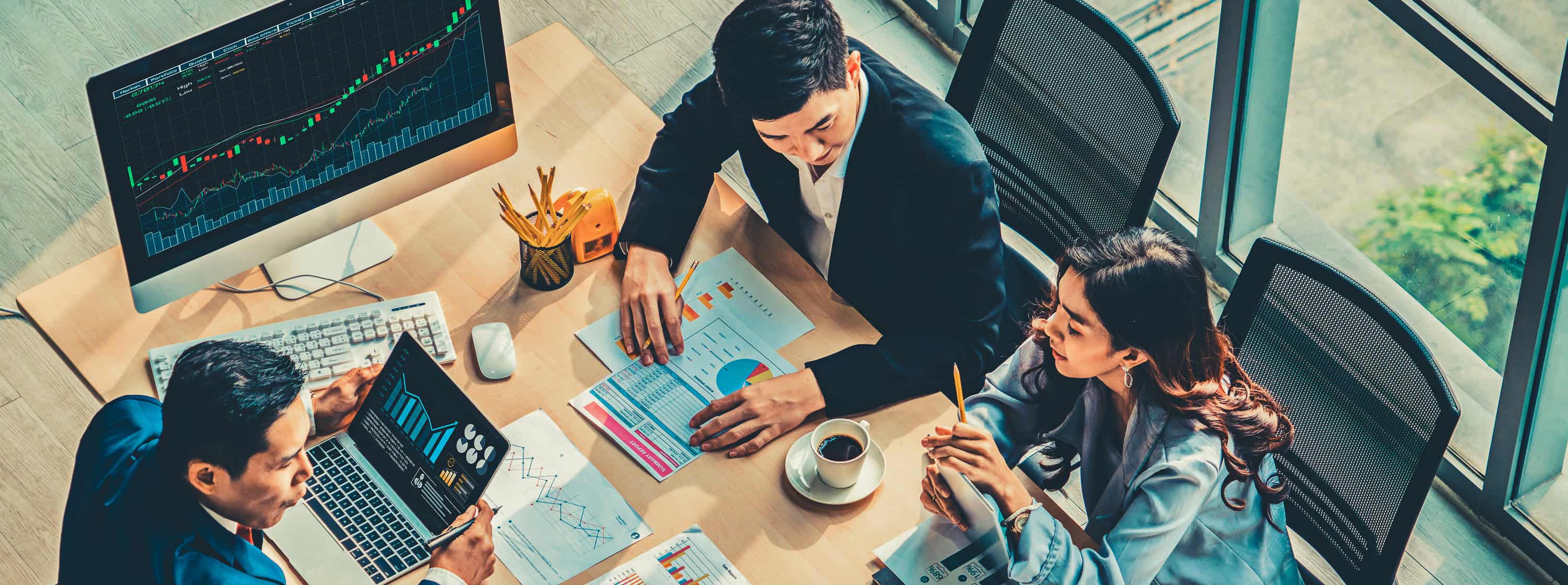 2 men and a woman discussing about stocks on a conference room with stock documents and computer