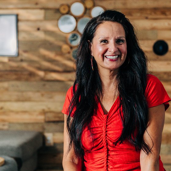 Meridian Member smiling while seated indoors, wearing a red top against a wood-panel wall.