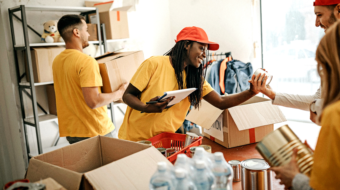 2 men and 2 women in yellow shirts with a notepad in hand and some boxes in front of them in a table