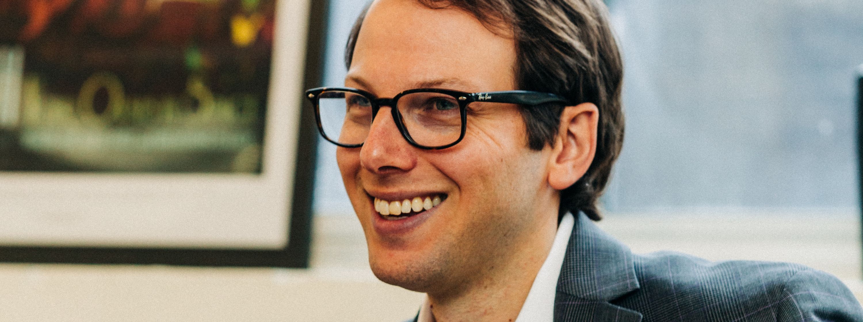 Close up of middle-aged male smiling, wearing glasses and a suit