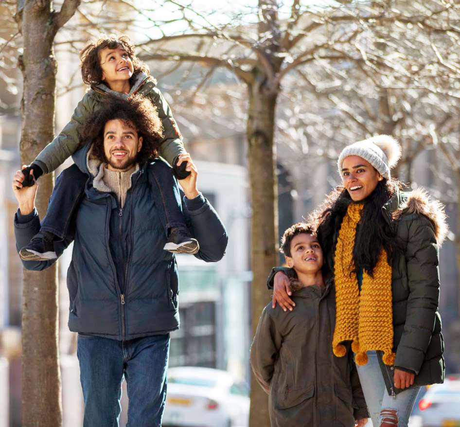 A man and woman are taking a winter walk with their two children. They all have medium tone skin and dark hair. 